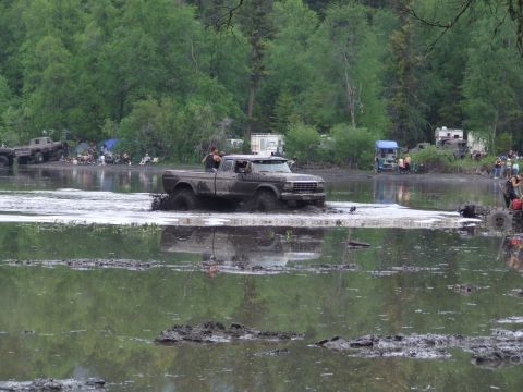 1990 Ford Bronco - A muddy pickup truck navigates through a waterlogged area during an outdoor event.