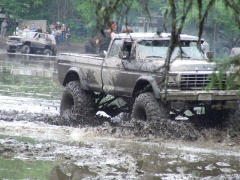 1990 Ford Bronco - Muddy 1979 Ford F-150 navigates water obstacle with another vehicle visible in the background.