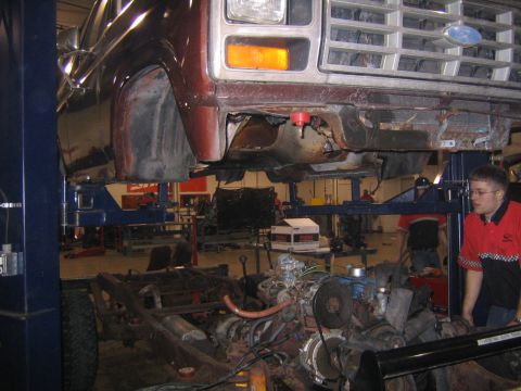 1982 Ford Bronco - A mechanic works on the exposed chassis and engine of a red Ford truck on a lift.