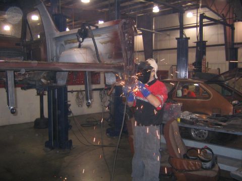 1982 Ford Bronco - A car body is suspended on a lift and being welded in a workshop, with another car visible in the background.