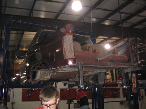 1982 Ford Bronco - A vehicle is undergoing repairs, elevated on a hydraulic lift in a garage setting.