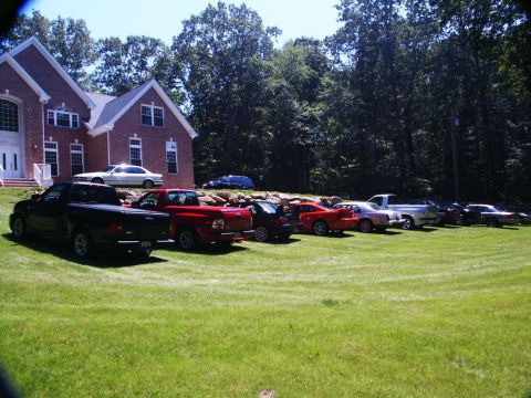 2001 Mercury Grand Marquis - A collection of vehicles are parked on a lawn in front of a large brick house on a sunny day.