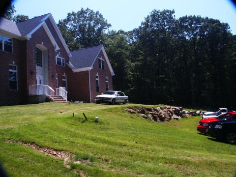 2001 Mercury Grand Marquis - A white sedan is parked on a lawn in front of a large brick house, with several other vehicles visible in the distance.
