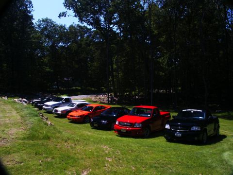 2001 Mercury Grand Marquis - A collection of vehicles are parked on a lawn in front of a wooded area on a sunny day.
