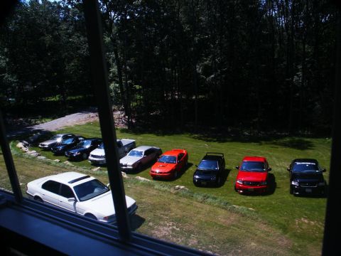 2001 Mercury Grand Marquis - A collection of vehicles are parked on a grassy area with trees in the background.