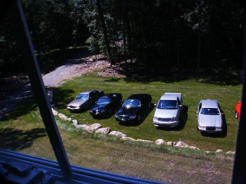 2001 Mercury Grand Marquis - A line of cars, including a 2001 Mercury Grand Marquis, are parked on a grassy area near a wooded lot.