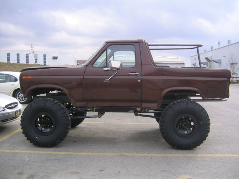 1982 Ford Bronco - A lifted brown 1980s Ford Bronco is parked next to another vehicle.