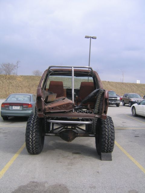 1982 Ford Bronco - This heavily modified SUV, stripped down and rusted, is viewed from the rear, showing its exposed frame and roll cage.