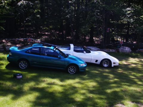 2001 Mercury Grand Marquis - Two cars, a teal coupe and a white sports car, are parked side-by-side on a grassy lawn surrounded by trees.