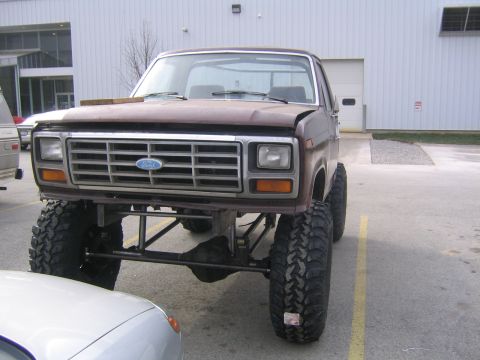 1982 Ford Bronco - A lifted brown Ford Bronco with a chrome grille is parked in front of a building.