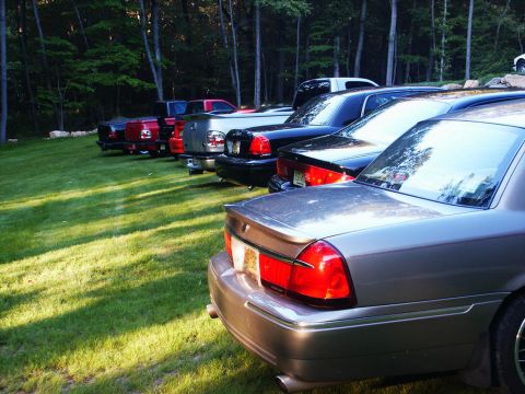 2001 Mercury Grand Marquis - Several cars are parked on a grassy lawn in front of a wooded area.