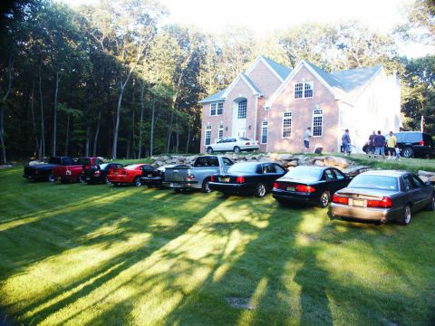 2001 Mercury Grand Marquis - A lineup of vehicles, including a 2001 Mercury Grand Marquis, are parked on the grass in front of a large brick house.