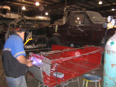 1982 Ford Bronco - A mechanic works on a red truck bed in a workshop, with a maroon Ford Bronco visible in the background.