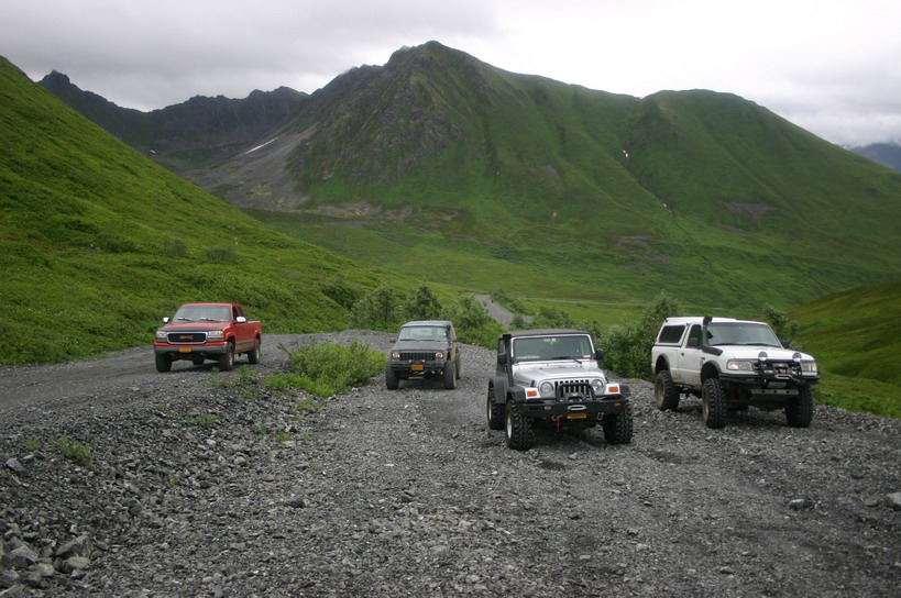 Four-wheel drive vehicles on a gravel road with green mountains in the background