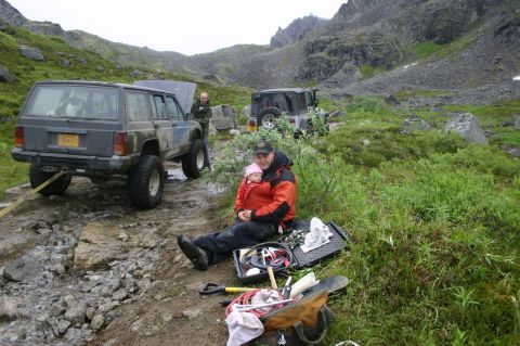 2003 Jeep TJ - Two Jeeps are parked on a rocky, off-road trail in a mountainous, grassy area.