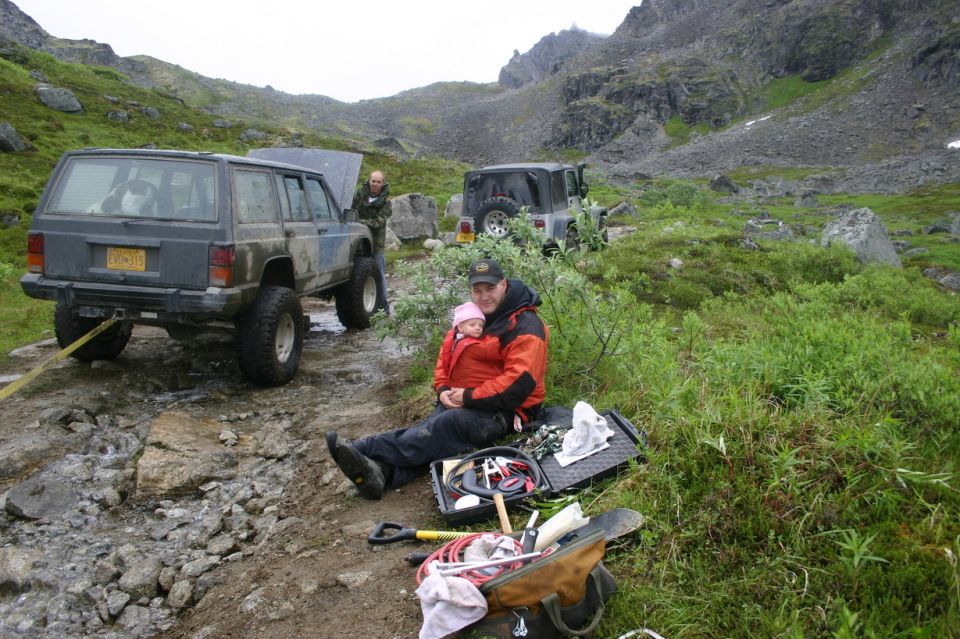 Dark gray Jeep Cherokee XJ with lifted suspension and off-road tires, rear view, attached to a yellow tow strap