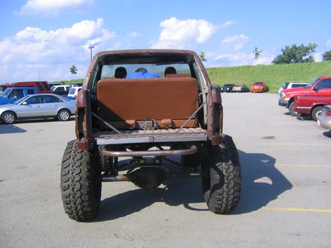 1982 Ford Bronco - This heavily modified SUV is parked in a lot with other vehicles under a partly cloudy sky.