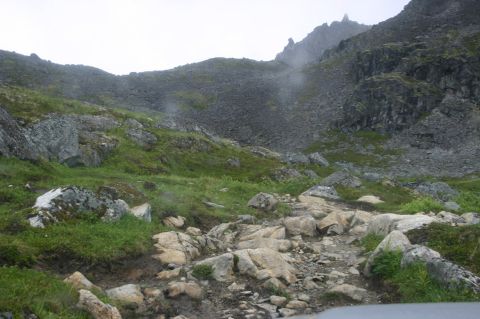 2003 Jeep TJ - A , mountainous landscape with a winding, rocky trail through sparse vegetation under a cloudy sky.