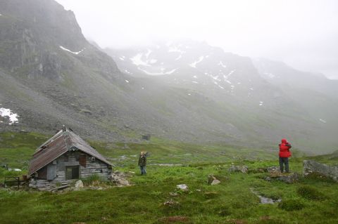 2003 Jeep TJ - A remote mountain landscape with a weathered cabin and two figures exploring the terrain.