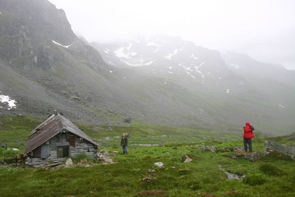 Rustic cabin in a misty mountain valley with two people observing the scenery