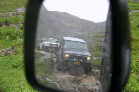 2003 Jeep TJ - Two SUVs navigate a challenging, rocky off-road path, captured in the reflection of a side mirror.