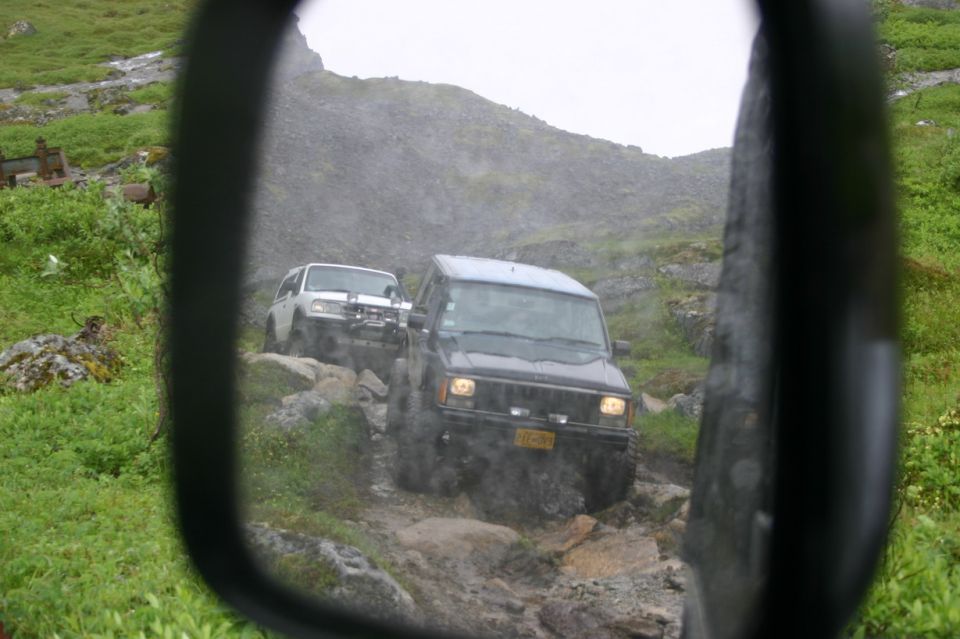 Two SUVs on a rocky off-road trail, viewed from a side mirror