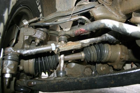 2003 Jeep TJ - The underside of a vehicle shows heavily soiled steering and suspension components, including a CV axle boot.