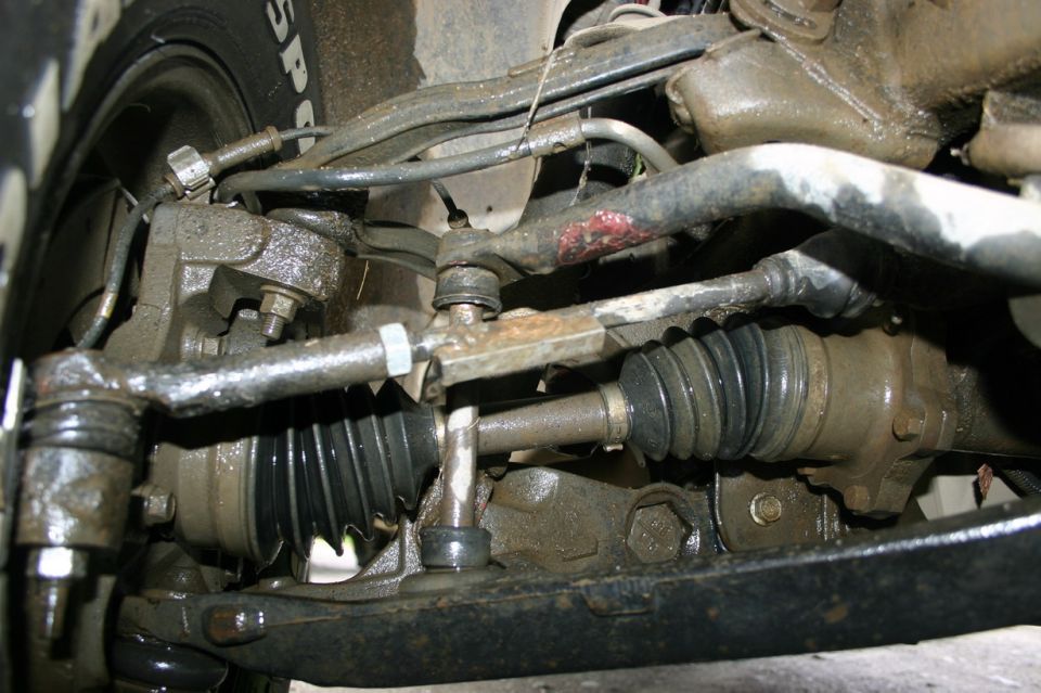 Close-up of dirty front suspension and steering parts, including tie rods and CV joint boots