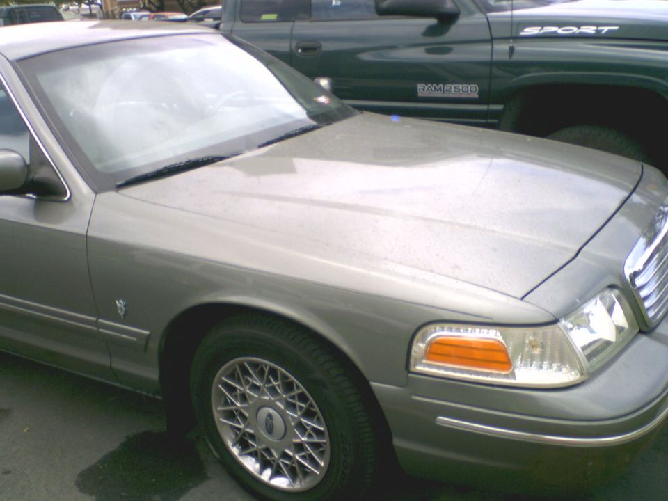 Front quarter of olive-gold Ford Crown Victoria with lacy chrome wheels beside Dodge Ram