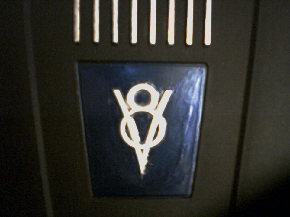 Chrome V8 emblem on a dark vehicle panel below vent slots