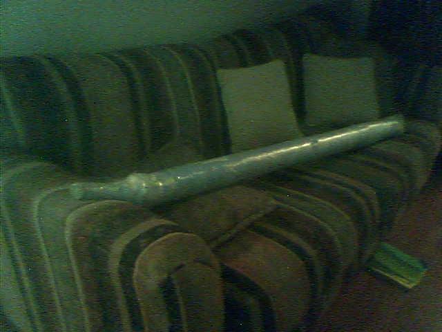 Long plastic-wrapped metal shaft resting across a striped couch indoors