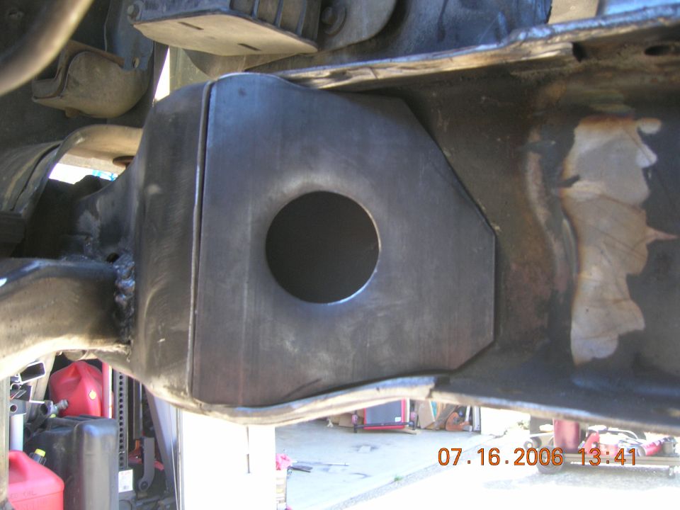 Fresh-welded custom steel frame bracket with large round hole, photographed from under the truck
