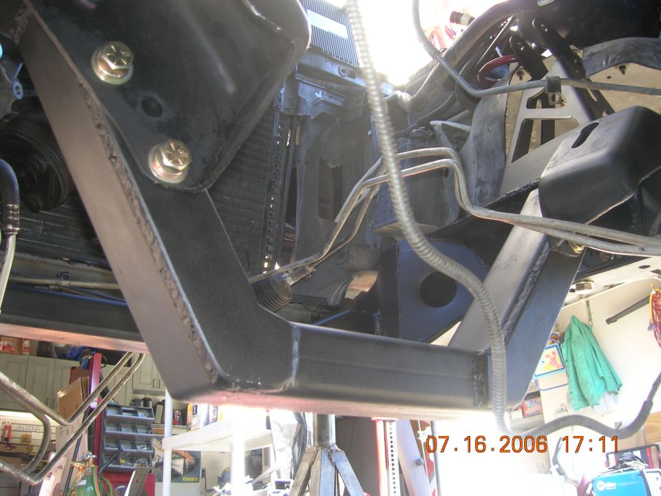 Underside view of black crossmember and radiator with bolts, vehicle on lift in garage