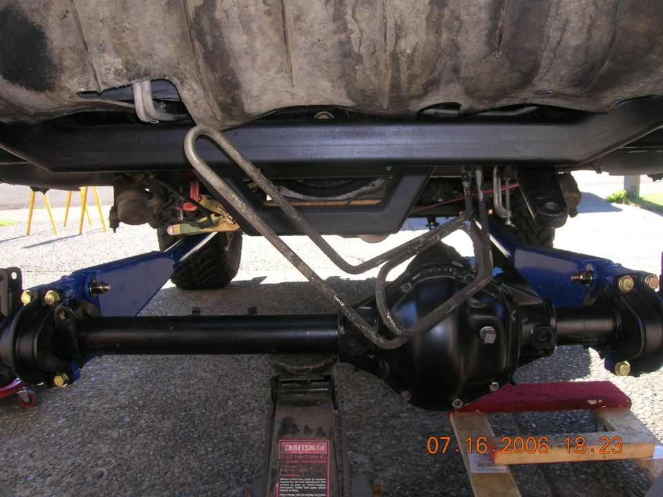 Black solid front axle on a floor jack being fitted under a lifted truck