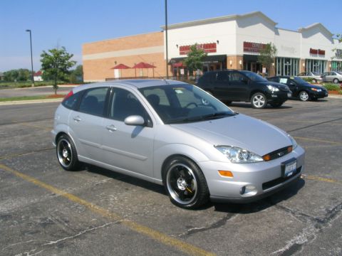 2003 Ford Focus - Silver 2003 Ford Focus hatchback with aftermarket rims parked in a lot.