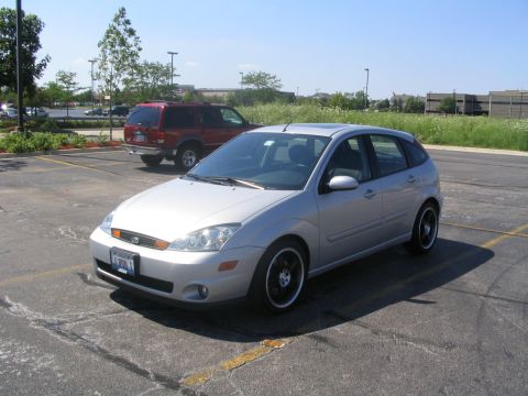 2003 Ford Focus - A silver hatchback is parked in a lot with a red SUV in the background.