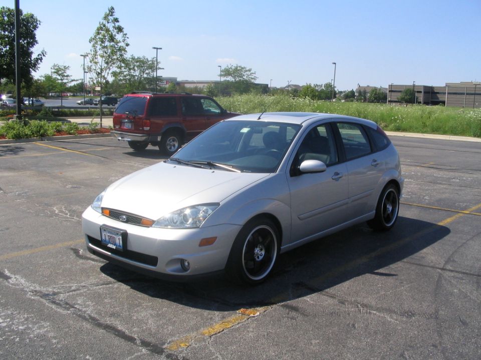 Silver hatchback parked in a lot, red SUV behind it