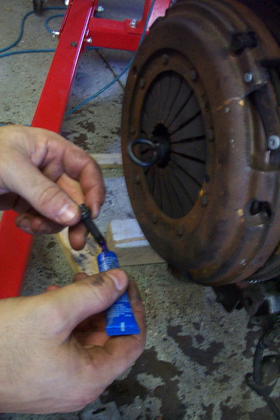 1995 Ford Taurus - A hand applies threadlocker to a bolt near a vehicle's clutch assembly, likely during an engine refresh or swap.