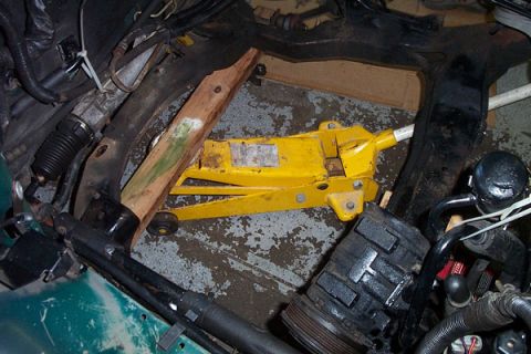 1995 Ford Taurus - A yellow jack is used to support wooden beams within the engine bay of a green vehicle.