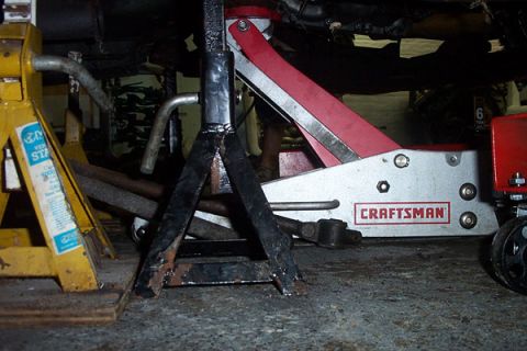 1995 Ford Taurus - Underneath view of a vehicle's engine bay, secured by jack stands and a floor jack for maintenance.