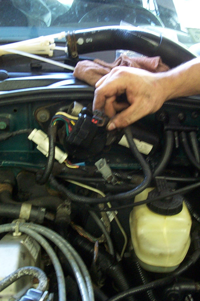1995 Ford Taurus - Close-up of a hand working on the wiring harness in a vehicle's engine compartment.
