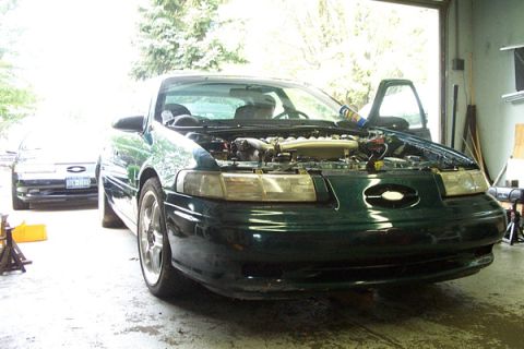 1995 Ford Taurus - A green Ford Taurus sits in a garage with its hood open, and another car is visible in the background.
