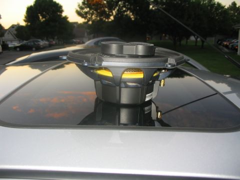 2003 Ford Focus - A car speaker is mounted on the sunroof of a silver vehicle, with trees and houses in the background.