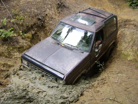 1987 Ford Bronco II - This SUV is deeply embedded in thick mud on an off-road trail, with only the top half visible.