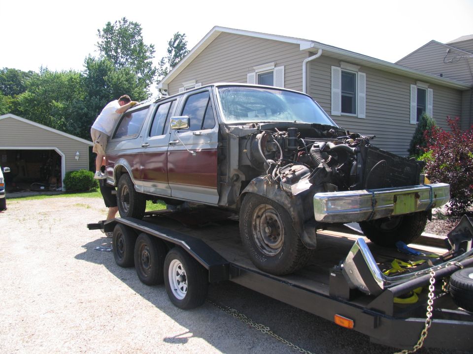 Maroon and silver SUV with exposed engine on a triple-axle trailer in a driveway