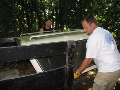 1986 Ford C-350 (Centurion Conversions) - Two men are seen loading a white camper shell onto a trailer in a wooded area.
