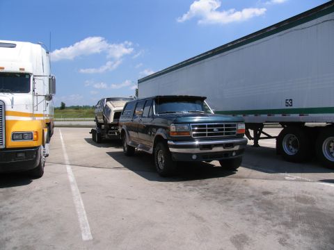 1986 Ford C-350 (Centurion Conversions) - Ford Bronco towing a car on a trailer, parked next to a semi-trailer truck.