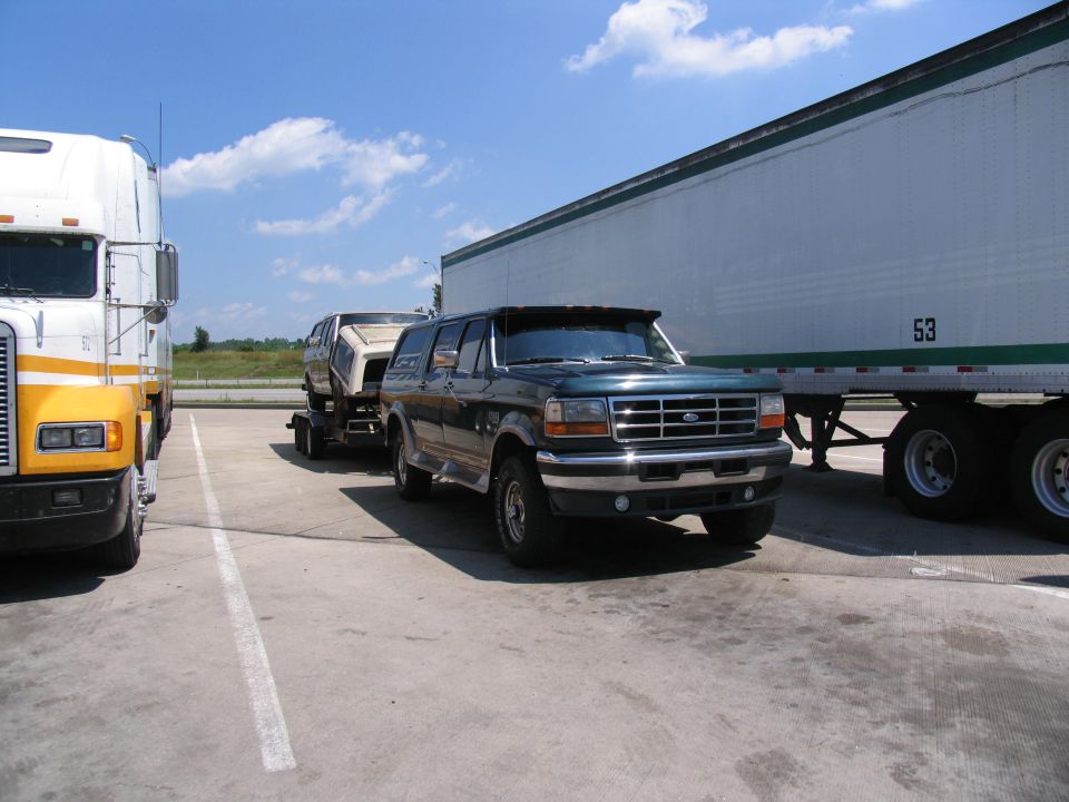 Dark green four-door Ford conversion truck towing a boat at a truck stop