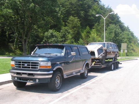 1986 Ford C-350 (Centurion Conversions) - A dark green Ford SUV tows a trailer carrying another SUV and its removable top.