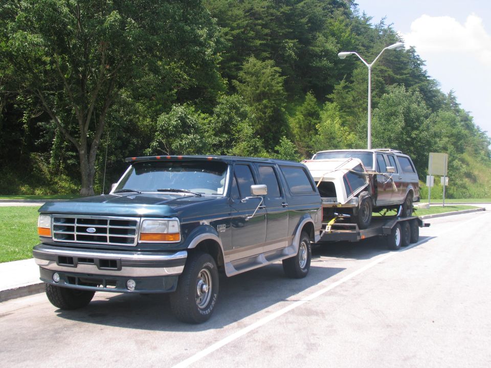 Dark green four-door Ford 4x4 SUV towing a trailer with a project SUV on it